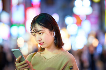 夜の繁華街でスマートフォンを見る若い女性