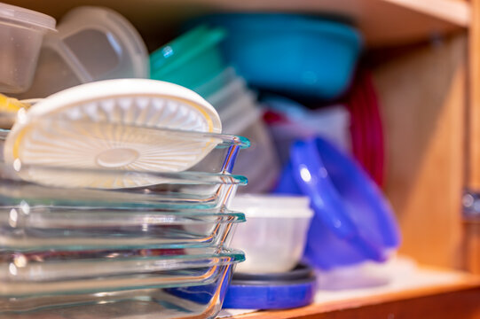 Narrow Depth Of Field Picture Of An Open Kitchen Cabinet With An Assortment Of Containers And Mismatched Lids Stacked.