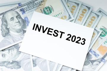 White card text Invest 2023 with dollors on the table