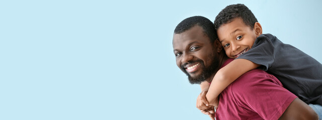 Obraz premium Portrait of happy African-American man and his little son on light blue background with space for text