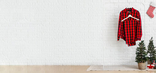 Rack with pajamas, Christmas trees and presents near white brick wall in room