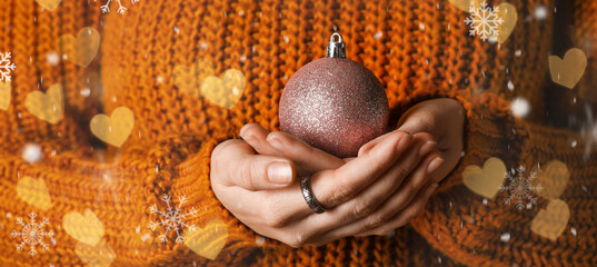 Woman in knitted sweater holding Christmas ball, closeup