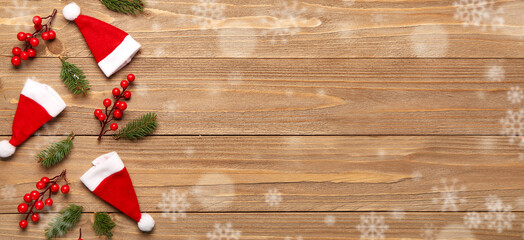 Santa hats, fir branches and red berries on wooden background with space for text