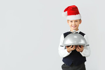 Cute little waiter in Santa hat on light background with space for text