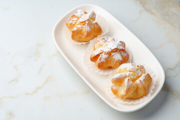 Homemade profiteroles with powdered sugar on white plate