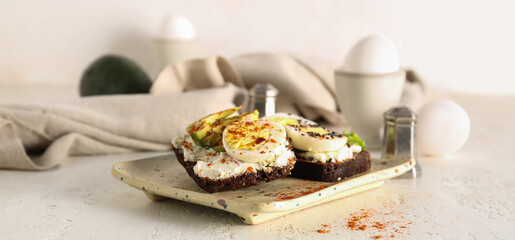 Tasty toasts with boiled eggs and avocado on white table