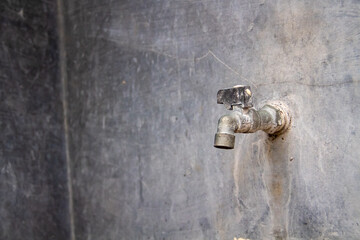 An old water faucet against a gray cement wall in the background