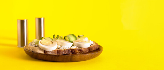 Tasty toasts with boiled eggs and cucumber on yellow background