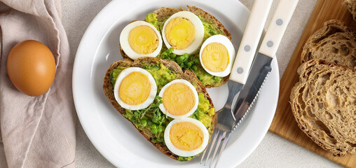 Plate of tasty toasts with boiled egg and avocado on light background, top view