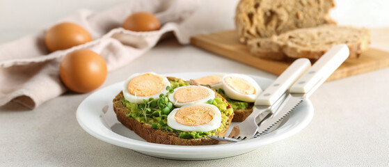 Tasty toasts with boiled eggs and avocado on light table