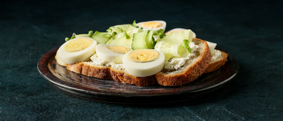 Plate of tasty toasts with boiled egg and cucumber on dark background