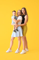 Happy lesbian couple with their little baby on yellow background