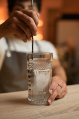 Professional bartender stirs cold cocktail with special bar spoon, close up. alcoholic drink in glass standing on the bar counter.