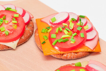 Crispy Cracker Sandwiches with Tomato, Sausage, Cheese, Green Onions and Radish on Cutting Board....