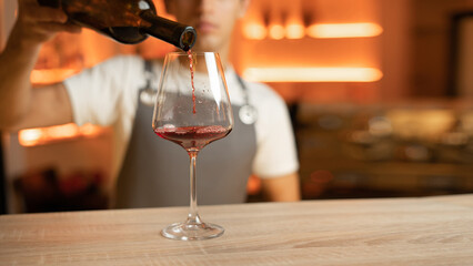 Bartender pouring red wine into a glass, close up. Hospitality and beverage concept.