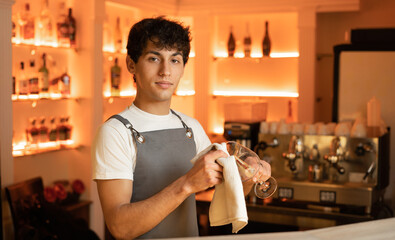 Arabic waiter cleaning a glass with a dish cloth wearing a gray apron.