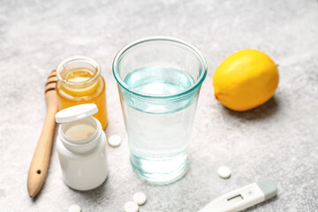 Glass of water, pills for sore throat, honey and lemon on grunge background