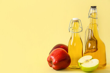 Bottles of apple cider vinegar and fruits on yellow background