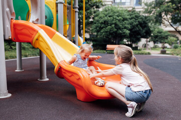 Cute blonde hair caucasian kids walking outdoor on playground at summer. Siblings having fun together