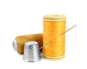 Thread spools, needle and thimble on white background