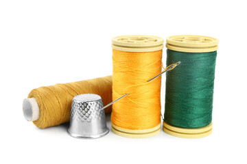 Thread spools, needle and thimble on white background