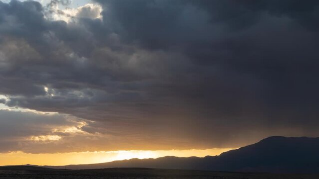 Time lapse video of the sun setting beyond Pine Valley mountain in Southern Utah with open desert below and dark brooding clouds above.