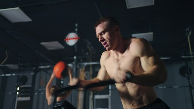 brawny man with naked torso is riding stationary bike in gym, portrait shot of handsome athletic guy