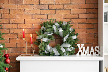 Christmas wreath and burning candles on mantelpiece near brick wall