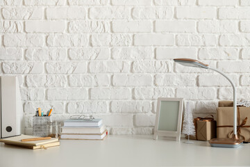 Workplace with frame, books, lamp and Christmas presents near white brick wall