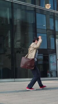Cheerful man walking and dancing near modern glass building. Vertical video