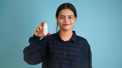 Portrait of a cheerful young woman holding asthma inhaler, Asian Indian girl with inhaler isolated over blue studio background, chronic obstructive pulmonary disease