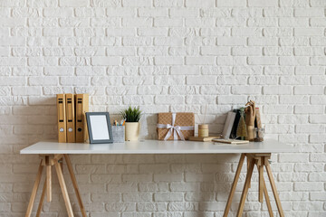 Workplace with frame, books and Christmas gift near white brick wall