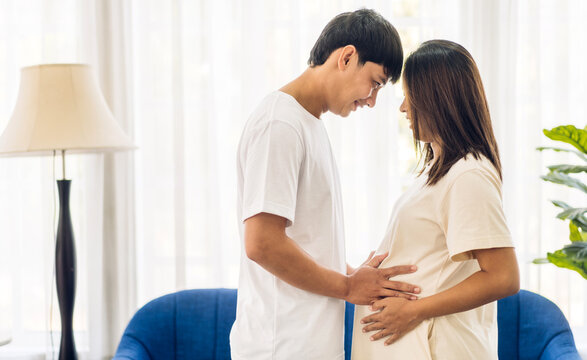 Romantic sweet asian couple husband hugging and smiling beauty asian pregnant wife.Man expecting with woman pregnancy hold to baby in belly at home