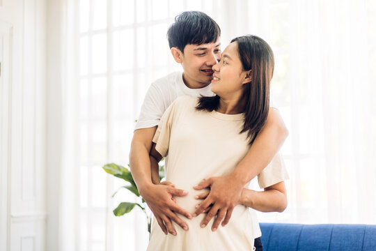 Romantic sweet asian couple husband hugging and smiling beauty asian pregnant wife.Man expecting with woman pregnancy hold to baby in belly at home