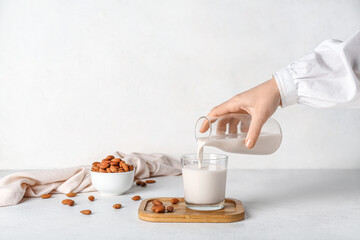 Woman pouring almond milk into glass on white table