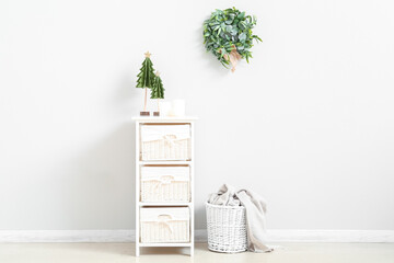 Chest of drawers with Christmas tree toys, basket and mistletoe wreath on light wall