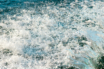 Waves on the sandy beach. Water background, blue sea water. Beautiful texture of sun glare on the water and sea foam.