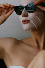 Young beautiful woman is resting in white fabric mask on her face and wearing black sunglasses