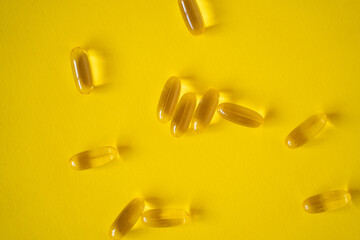 Transparent gel fish oil capsules with omega-3 and vitamin D isolated on yellow background. Healthy diet concept.