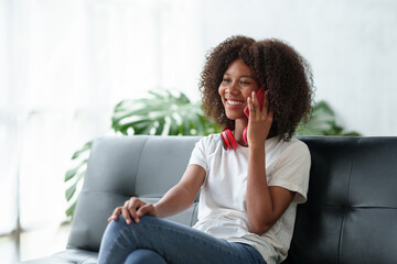 Young woman sitting on the sofa in the living room using mobile phone to talk on vacation. Woman using smartphone at home.