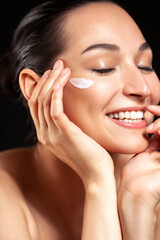 Young beautiful happy woman applying cream on her face