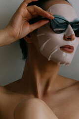 Young beautiful woman is resting in white fabric mask on her face and wearing black sunglasses