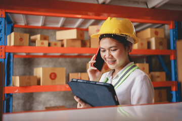 Asian female supervisor using mobile phone to chat with customers and check inventory with tablet to check product quality.