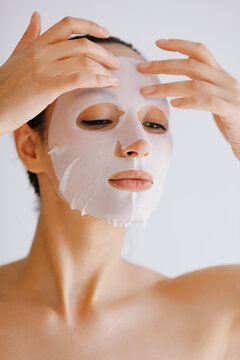 Young woman applies white sheet mask to her face