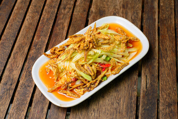 Papaya salad and crispy fish on the wooden background.