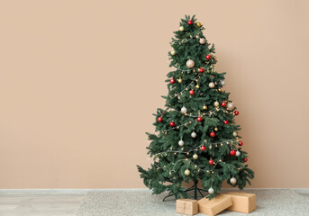 Glowing Christmas tree with presents near beige wall