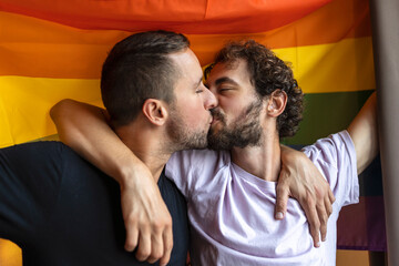 Passionate gay couple making out with lgbtq flag in the background. Young gay couple bonding fondly indoors.