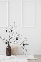 Vase with tree branches, Christmas balls and pillow near light wall