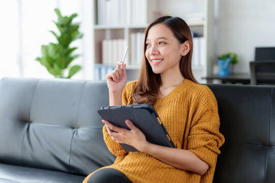 Bright and cute Asian woman using tablet to listen to music and other entertainment Relaxing at home happily watching movie and playing game at home.