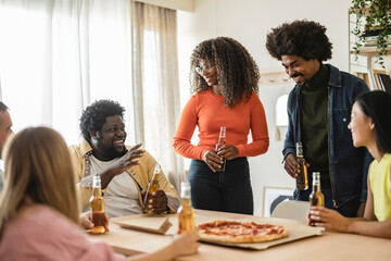 Group of young multiethnic friends having fun at party with pizza and bottles of drink celebrating...